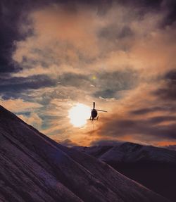 Low angle view of silhouette airplane flying over mountains against sky