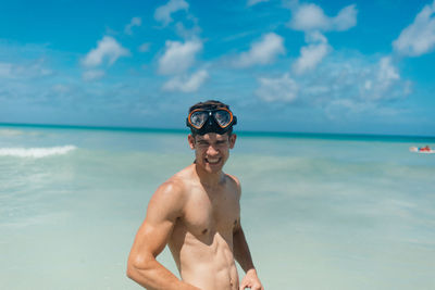 Portrait of shirtless man standing at beach against sky