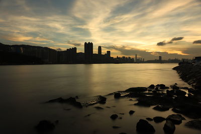 Sea by buildings against sky during sunset