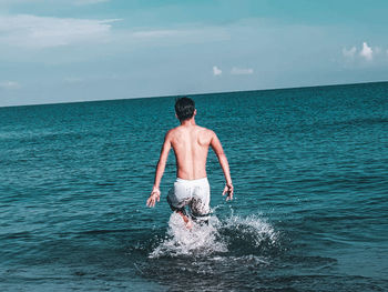 Rear view of shirtless man in sea against sky