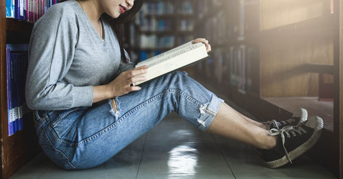 Midsection of woman reading book while sitting on tiled floor