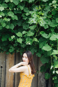 Beautiful woman standing by wooden wall against tree