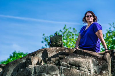 Portrait of young woman against retaining wall against blue sky