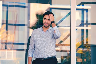 Portrait of young man standing against glass wall