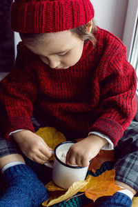 Boy a child in a red sweater and a knitted hat sits at the window on the windowsill
