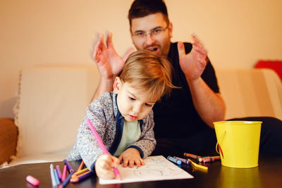 Happy man playing with son making drawing on table at home