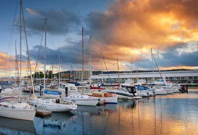 Boats moored in harbor at sunset