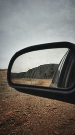 Close-up of side-view mirror against sky