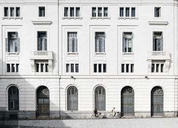 Couple riding e-bkes in the city passing a building