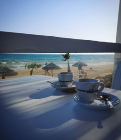 Empty table by sea against clear blue sky