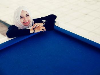 High angle portrait of smiling young woman standing by pool table