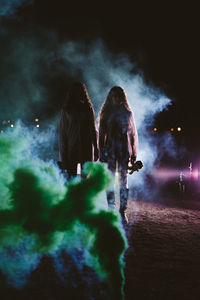 Female friends standing amidst smoke on land at night