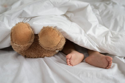 Low section of baby with teddy bear relaxing on bed