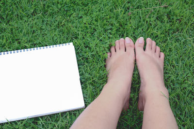 Low section of woman by blank spiral notebook on grass