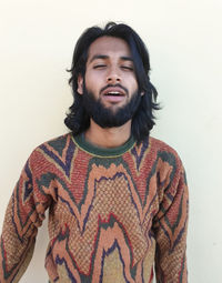 Portrait of young man standing with making face against white background