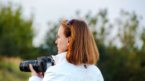 Rear view of woman with dslr against trees