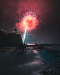 People on beach against firework display at night