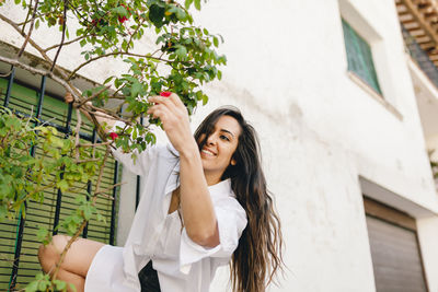 Portrait of smiling woman holding plant against building