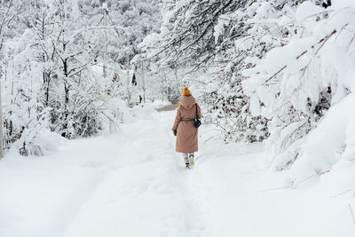 Back view of a woman in a coat and a yellow shake walking along a snowy path.