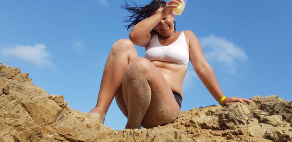 Low angle view of young woman sitting against sky