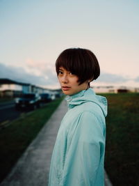 Portrait of woman with short hair standing on footpath against sky during sunset