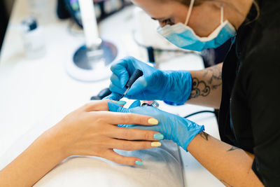 Midsection of beautician wearing mask applying nail polish to woman