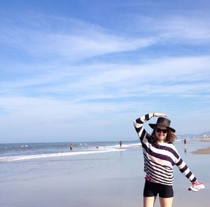 Happy woman standing on shore at beach against sky