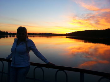 Silhouette woman standing by railing against sky during sunset