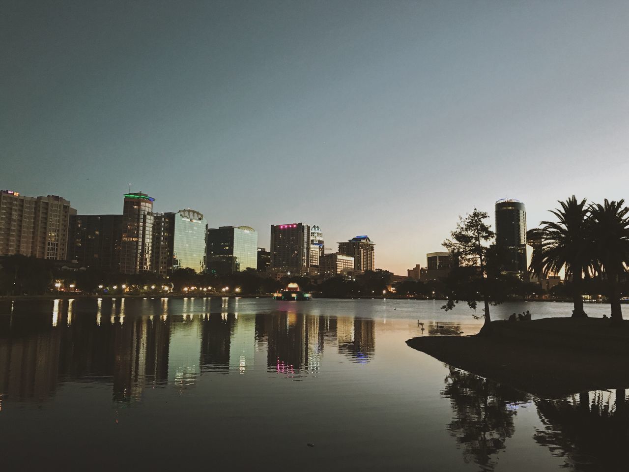 architecture, building exterior, built structure, water, skyscraper, reflection, city, palm tree, clear sky, modern, waterfront, tree, travel destinations, outdoors, growth, no people, cityscape, illuminated, night, sky