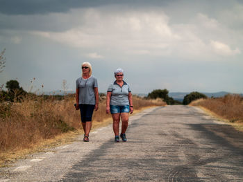 Female friends walking on road against cloudy sky