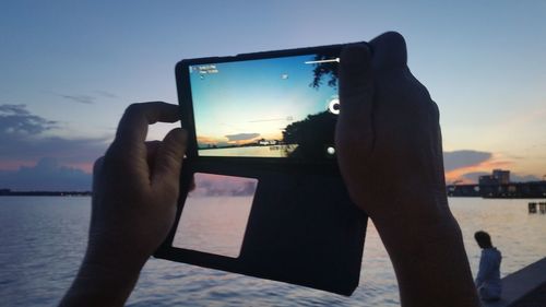 Man photographing through smart phone against sky during sunset