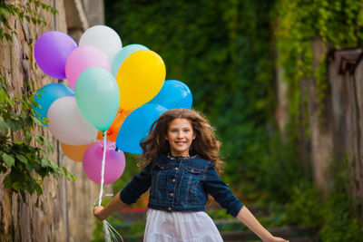 Portrait of smiling girl holding balloon running outdoors