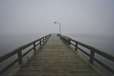 Pier over water against foggy sky