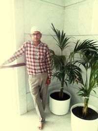 Portrait of smiling man standing by potted plant at home