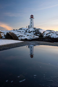 Lighthouse by sea against sky during sunset