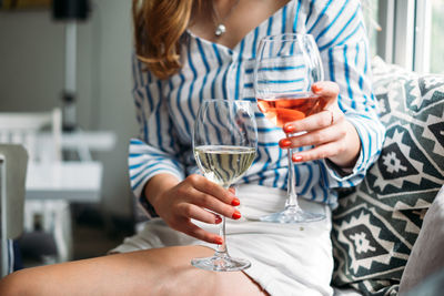 Midsection of woman holding wineglasses while sitting on sofa