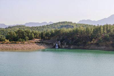 Tranquil forest lake with rocky waterfall and mountainous horizon