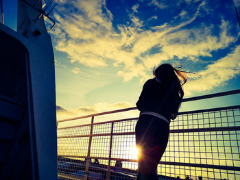 Rear view of silhouette woman standing by railing against sky