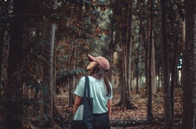 Rear view of man standing by tree trunk in forest