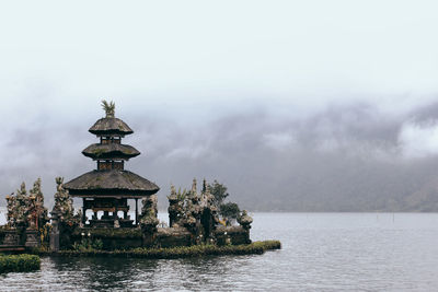 Illuminated building by lake against sky