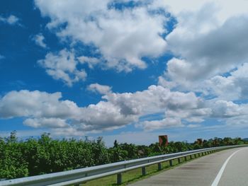 Empty road by trees against sky