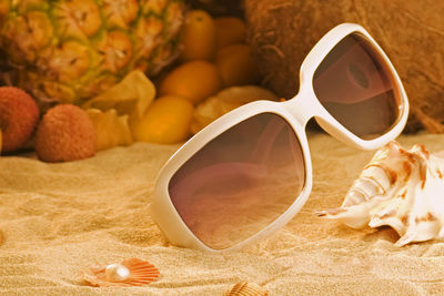 Close-up of sunglasses on sand against fruits
