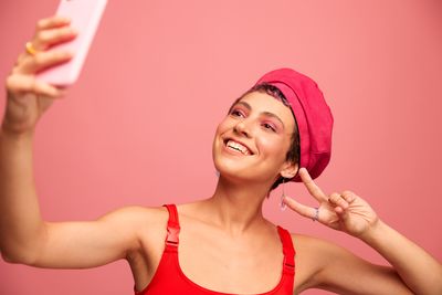 Portrait of young woman wearing hat while standing against pink background