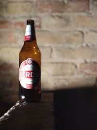 Close-up of beer bottle on table against wall