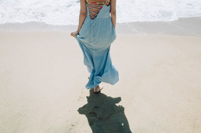 Low section of woman walking at beach on sunny day