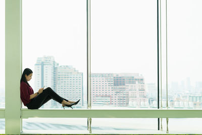 Side view of woman sitting on glass window