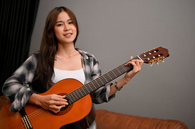 Portrait of young woman playing guitar against white background