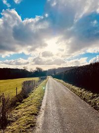 Empty road amidst field against sky