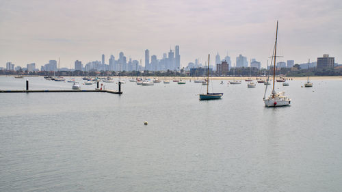 Sailboats on sea by buildings in city against sky