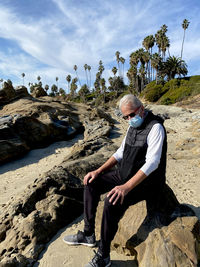 Man sitting on rock against sky